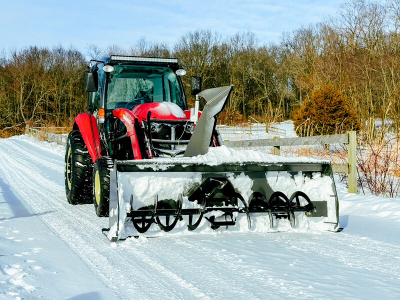 Snow blower mounted to the loader of a red Yanmar tractor